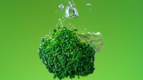 flor de brócoli caído en el agua hace burbujas y se hunde sobre fondo verde, cámara lenta y macro