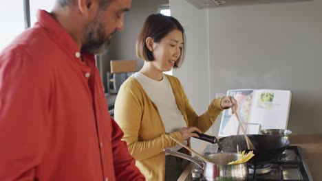 happy diverse couple cooking together, mixing ingredients in pan in kitchen