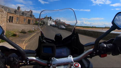 biker riding a motorcycle to a harbour in scotland with clear blue skies and yachts in the marina