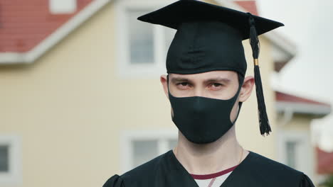 portrait of a graduate in a protective mask wearing a robe and a graduate cap 1