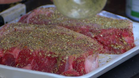 a hand pours spices all over an already covered rib eye steak