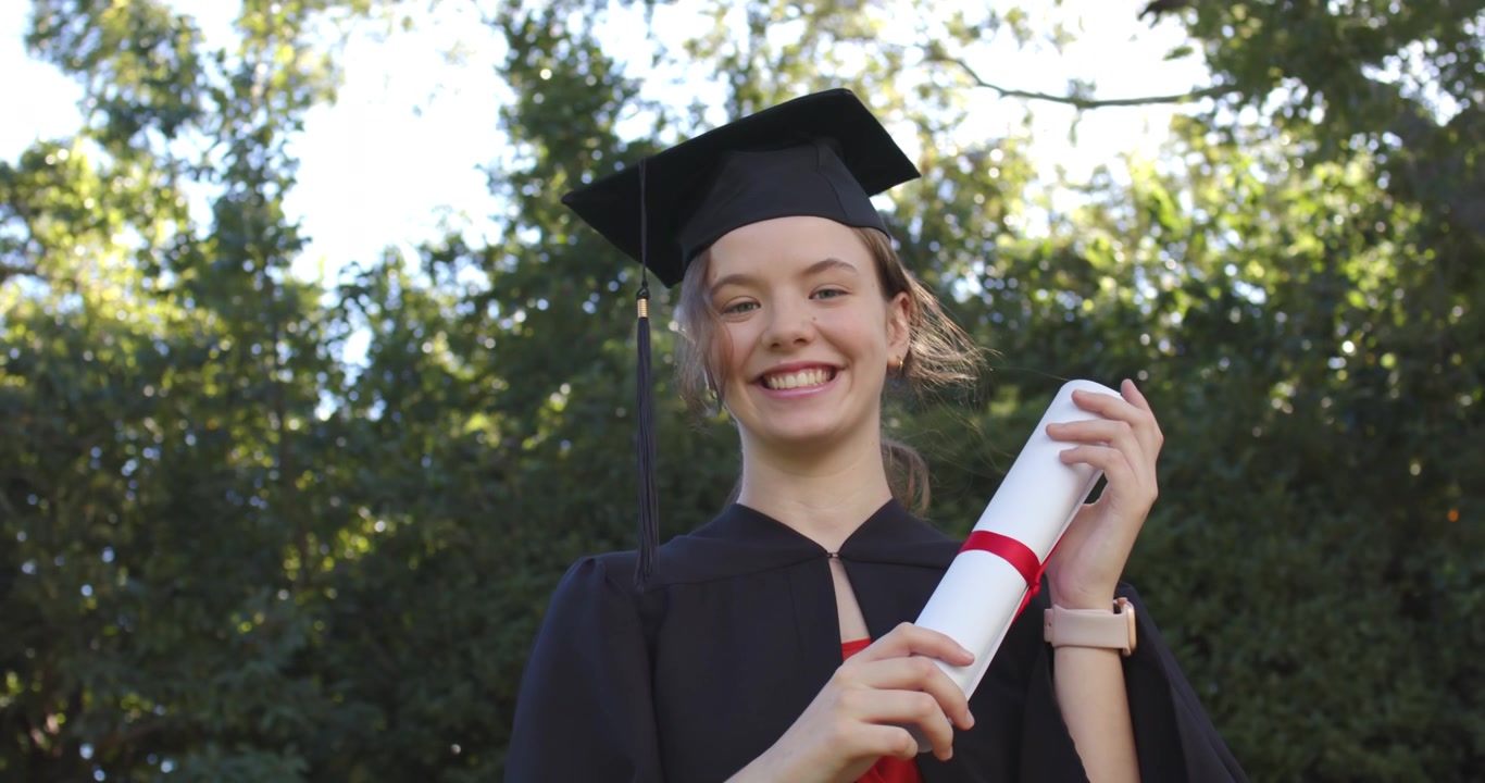 Laureata in toga che tiene un diploma con nastro, aggiustando la presa mentre sorride dopo la cerimonia all'aperto.