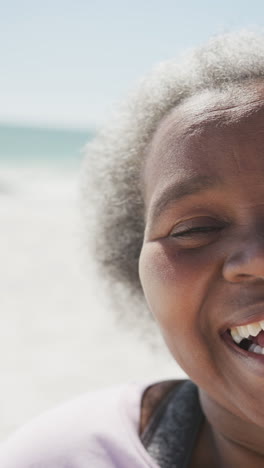 vertical video of portrait of happy senior african american woman smiling at beach, in slow motion