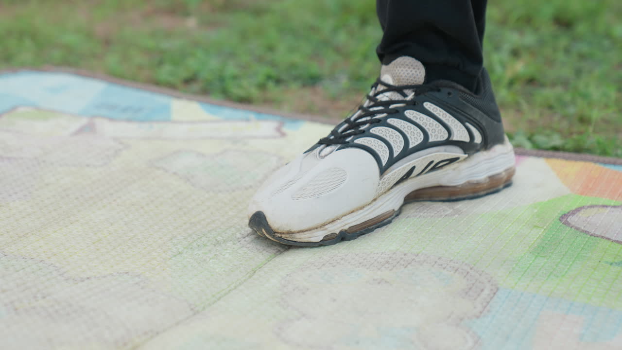 Preparazione concentrata alla corsa. Sneaker sull'erba da esterno. Vista dettagliata di una scarpa atletica su terreno erboso all'aperto. Primo piano di una scarpa da ginnastica sportiva a terra con lacci neri durante un esercizio di allenamento.
