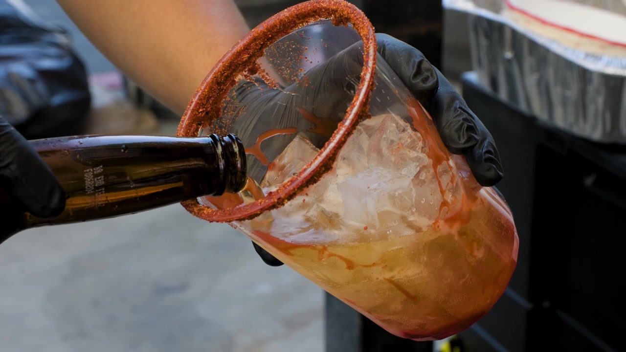 Filmato di preparazione di bevande che mostra un uomo versare birra in una tazza per michelada durante la preparazione di una gustosa bevanda messicana michelada.