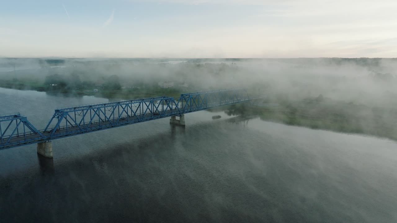vista aérea del puente de acero sobre el río lielupe en una soleada mañana de verano, niebla que se eleva sobre el río, coches circulando, amplia toma de avión no tripulado moviéndose hacia adelante, inclinándose hacia abajo