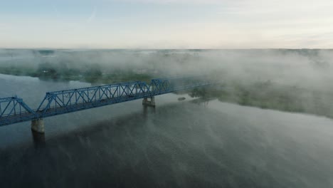 aerial establishing view of the steel bridge over lielupe river on a sunny summer morning, fog rising over the river, cars driving, wide drone shot moving forward, tilt down