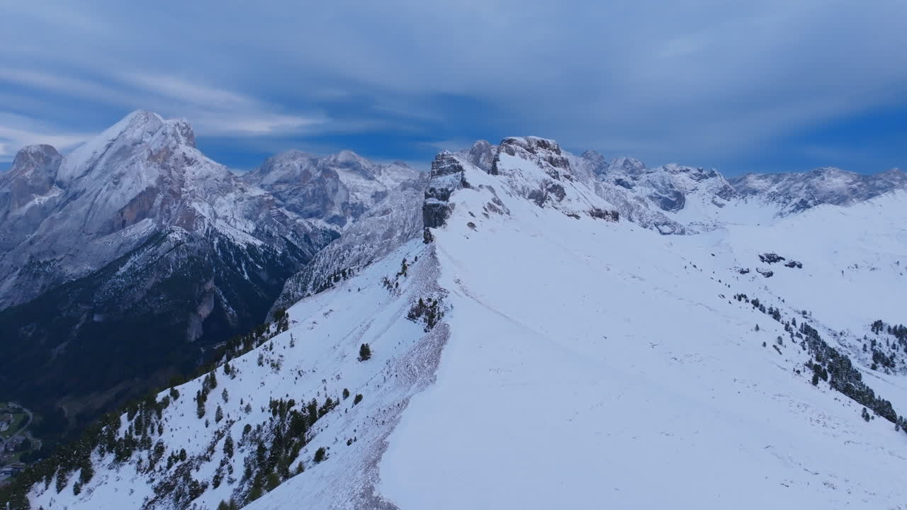 imágenes aéreas volando sobre el pico de una montaña que está cubierta de nieve fuera de la ciudad de canazei, italia.