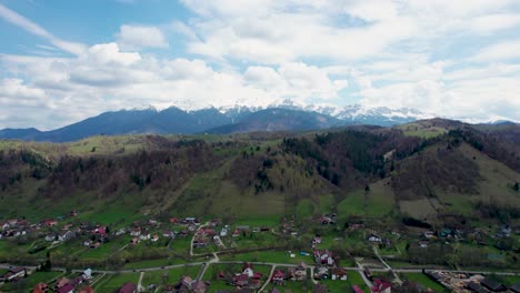 Das-Majestätische-Bucegi-Gebirge-–-Ein-Atemberaubender-Drohnenblick-Auf-Schneebedeckte-Gipfel,-Ein-Malerisches-Bergdorf-Und-Ruhige-Grüne-Felder-Im-Herzen-Von-Rumäniens-Siebenbürgen,-Moieciu,-Rucar,-Bran