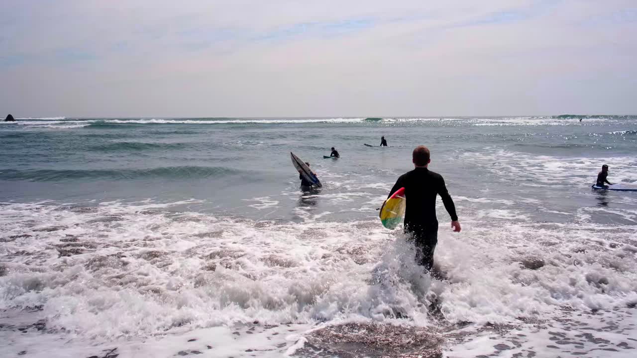 joven corriendo hacia el mar, motivado para surfear, mientras los niños toman clases de surf