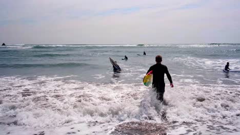 junger mann rennt zum meer, motiviert zum surfen, während die kinder surfunterricht nehmen