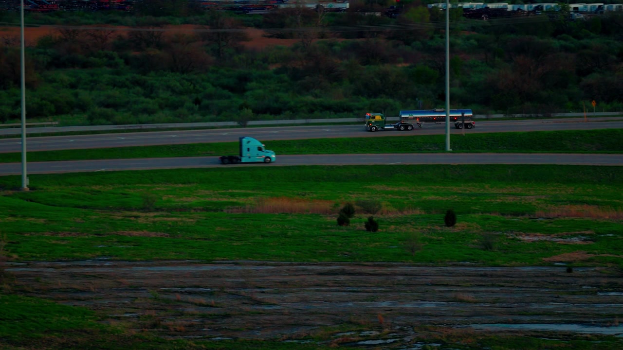 A single cabover fuel tanker drifts along a still, near-empty highway in fading dusk light, green fields and dim trees evoking a quiet, solitary Midwest evening.