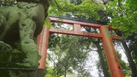 Vista-De-ángulo-Bajo-De-La-Gran-Puerta-Torii-Roja-Junto-A-La-Estatua-En-El-Bosque-De-Nara