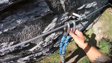 pov shot of a young man clipping on the safety carabiners one at a time during his rock climbing hike in switzerland with the bright high noon sunlight