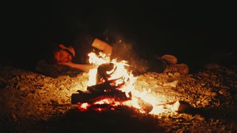 tired man lying on dusty ground in glow of blazing campfire in desert at night