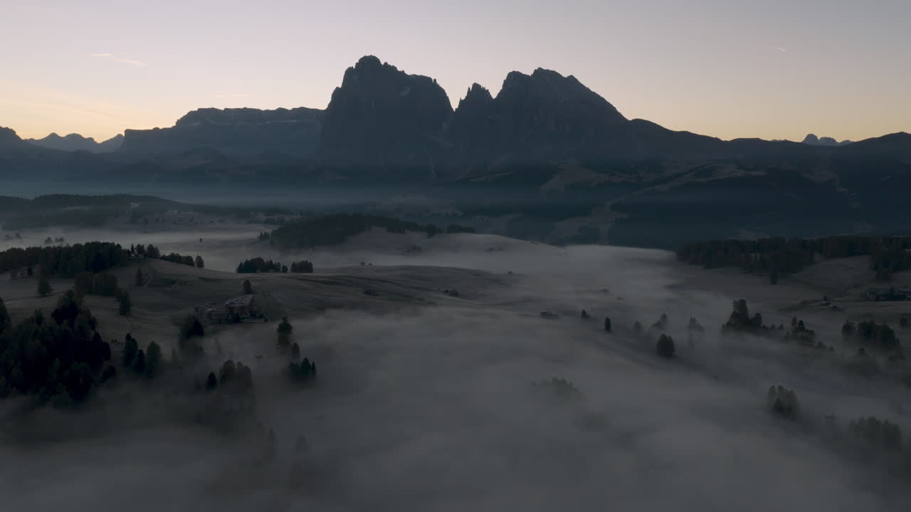 Cinematic aerial view of Sassolungo massif rising above a sea of clouds at sunrise, serene Alpe di Siusi alpine landscape in the Dolomites, Italian Alps travel destination