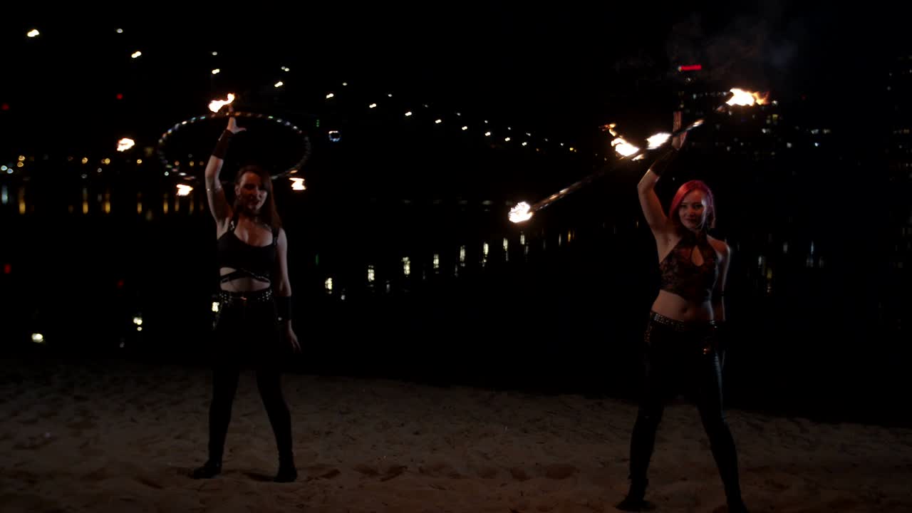 mujeres jóvenes girando el fuego hula hoops por encima de la cabeza