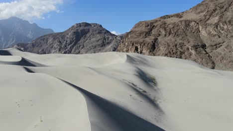 Drone-Aéreo-Volando-Hacia-Atrás-Revelando-Grandes-Dunas-De-Arena-En-El-Frío-Desierto-De-Skardu-Pakistan-Con-Vistas-A-Grandes-Montañas