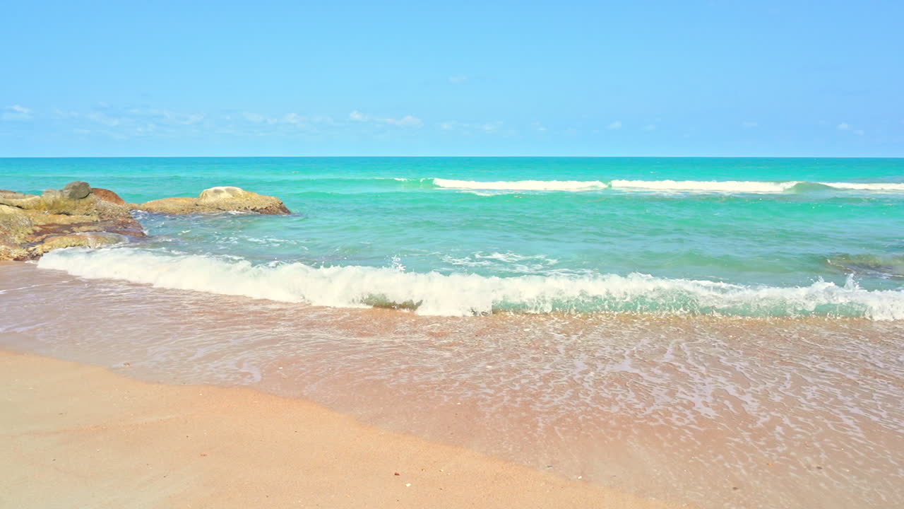 파도가 해변의 모래 위로 밀려오고 얕은 물에 있는 큰 바위