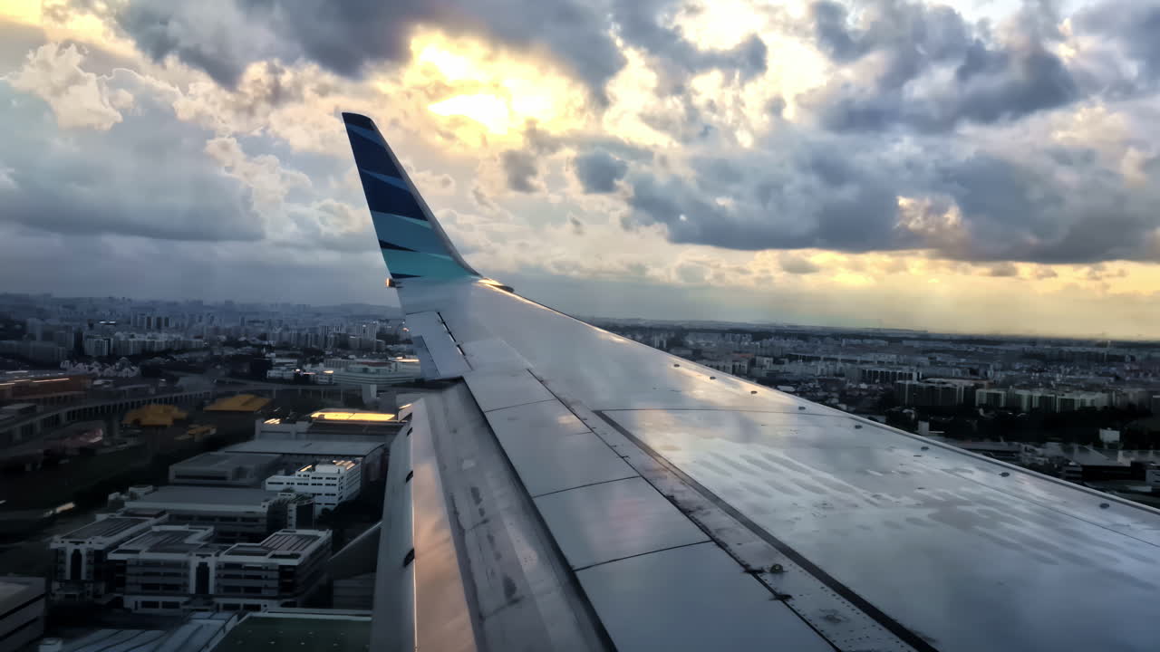 A dramatic view from a passenger airplane window, looking over the wing of a Garuda Indonesia jet as it lands in Singapore at sunset with a cloudy, beautiful sky