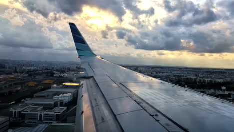 a dramatic view from a passenger airplane window, looking over the wing of a garuda indonesia jet as it lands in singapore at sunset with a cloudy, beautiful sky