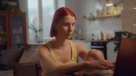 red-haired girl typing on laptop at table in living room