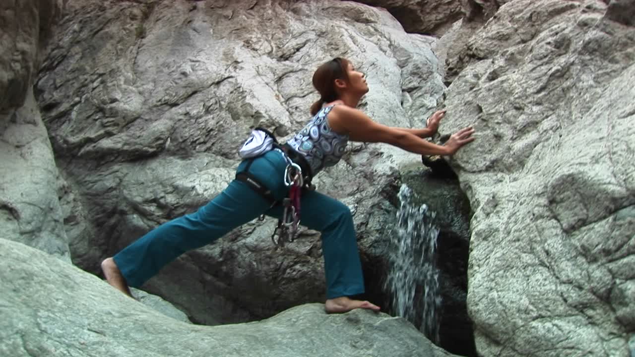 plano medio de una mujer haciendo estiramientos junto a una pequeña cascada en una roca de granito
