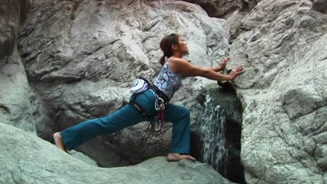 mediumshot of a woman doing stretches next to a small waterfall on a granite rockface