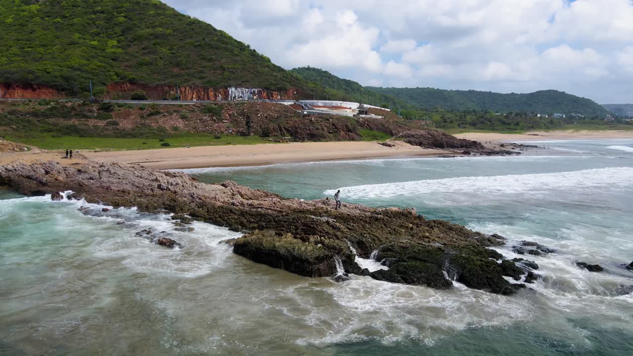Aerial drone shot of a striking rock formation standing tall in the ocean, with Vizag’s coastal beauty in the distance.