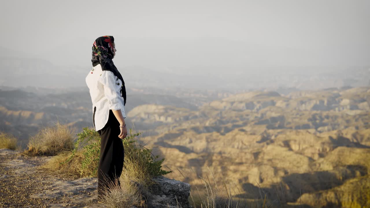 Muslim woman raising arms in freedom on mountain top at sunset