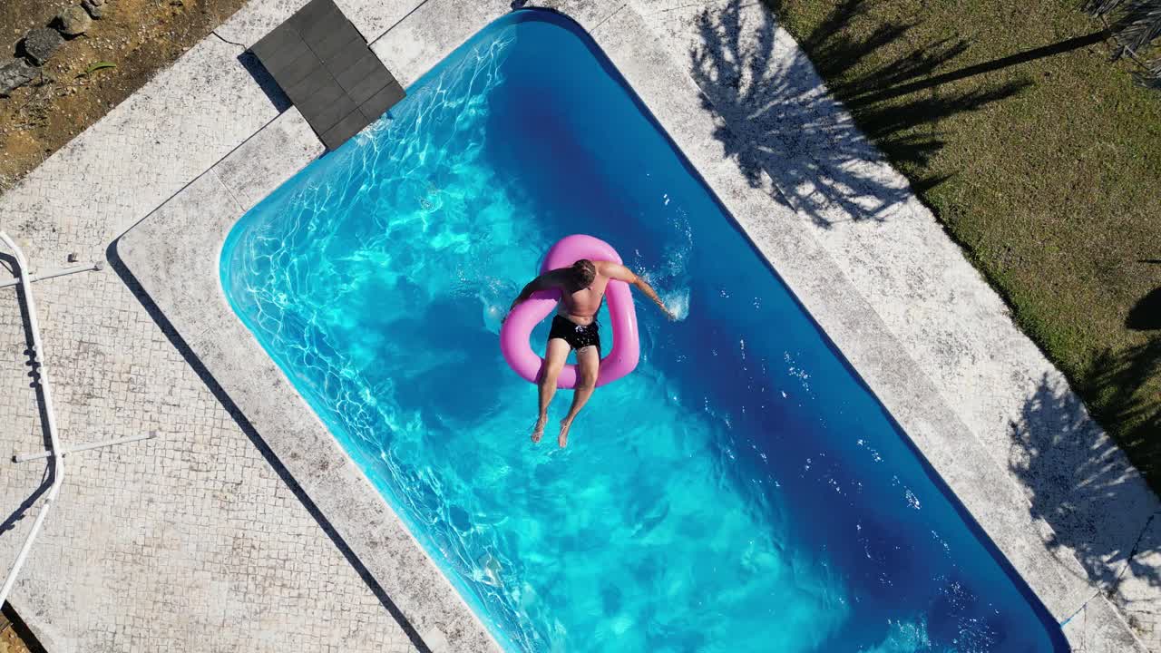 Seen from above a boy on a pink heart-shaped buoy playing with a ball at pool