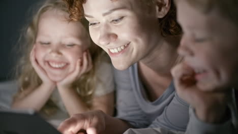 mother lying in bed with her son and daughter reading a fairy tale reading on smartphone