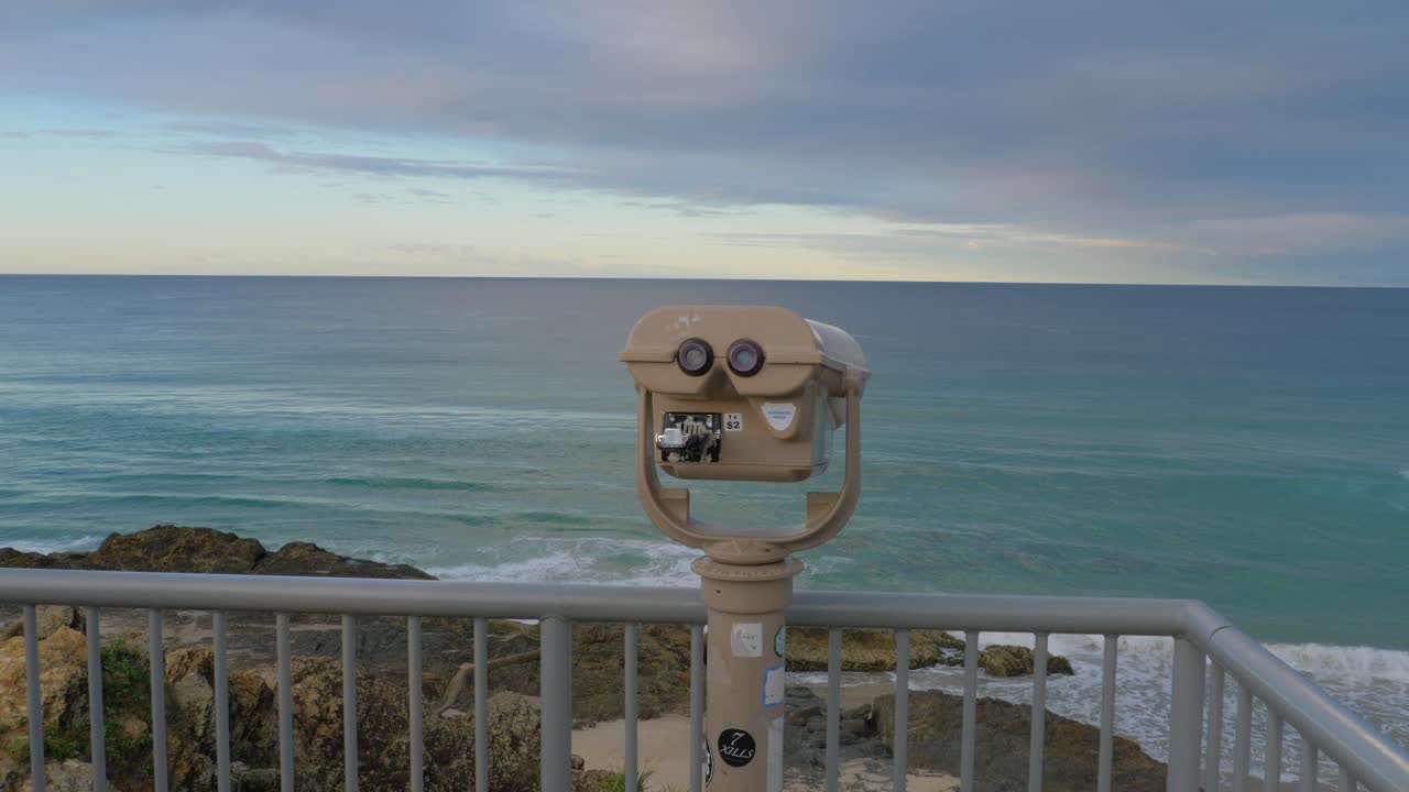 telescopio de binoculares en el mirador de la roca del elefante - mar tranquilo desde la playa de currumbin en la puesta del sol - costa de oro, queensland, australia