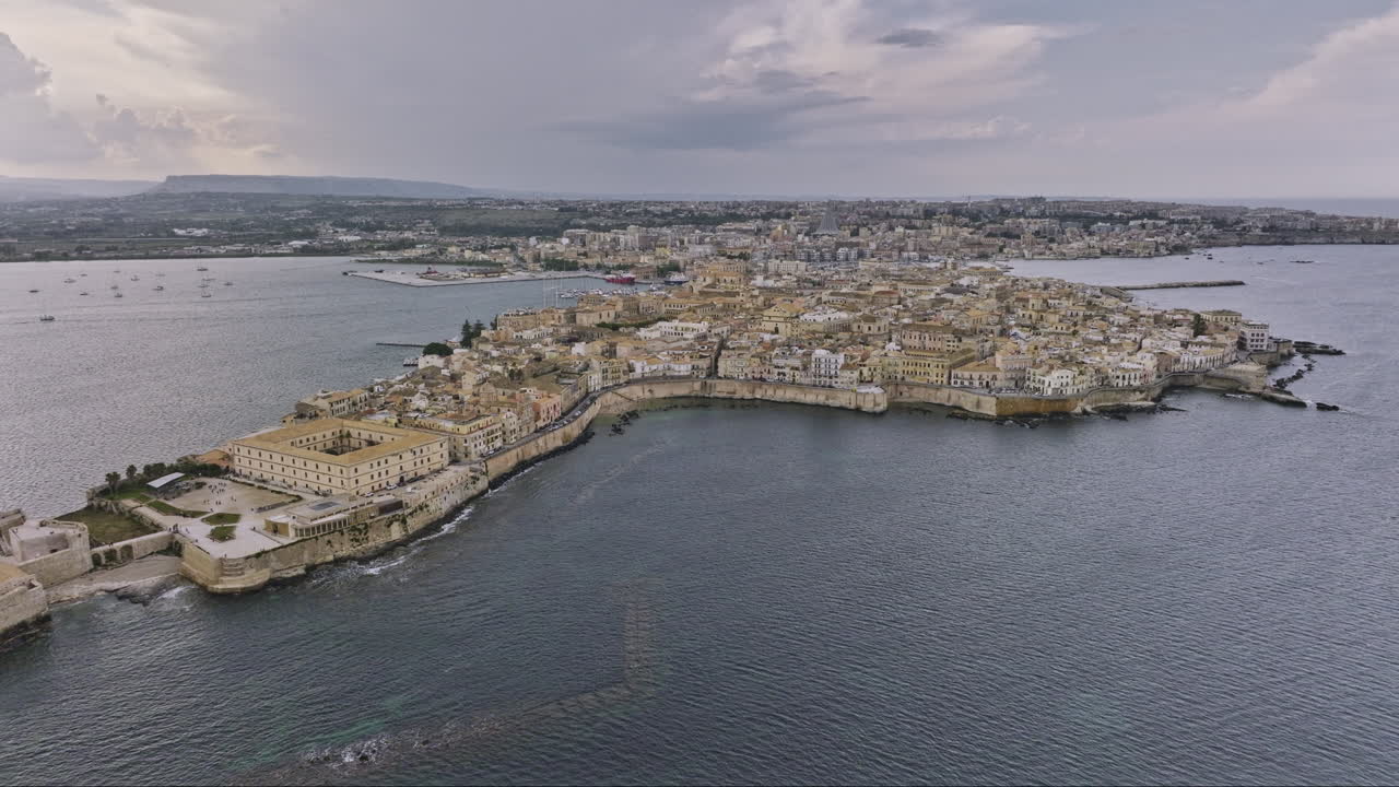 Syracuse Italy Aerial v2 establishing drone flyover capturing ancient old city of Ortigia Island with historical stone buildings and island bounded by Ionian sea - Shot with Mavic 3 Cine - June 2023