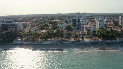 Right-trucking-aerial-drone-shot-of-the-tropical-Bessa-beach-in-the-capital-city-of-Joao-Pessoa,-Paraiba,-Brazil-with-people-enjoying-the-ocean-surrounded-by-palm-trees,-beach-houses,-and-apartments