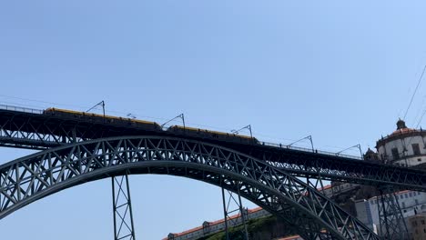 Bottom-up-shot-of-riding-train-on-top-of-Dom-Luís-I-Bridge-crossing-river-Douro-against-blue-sky