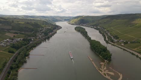 long cargo ship traveling along the rhine river between lush meadows and vineyards on a sunny day