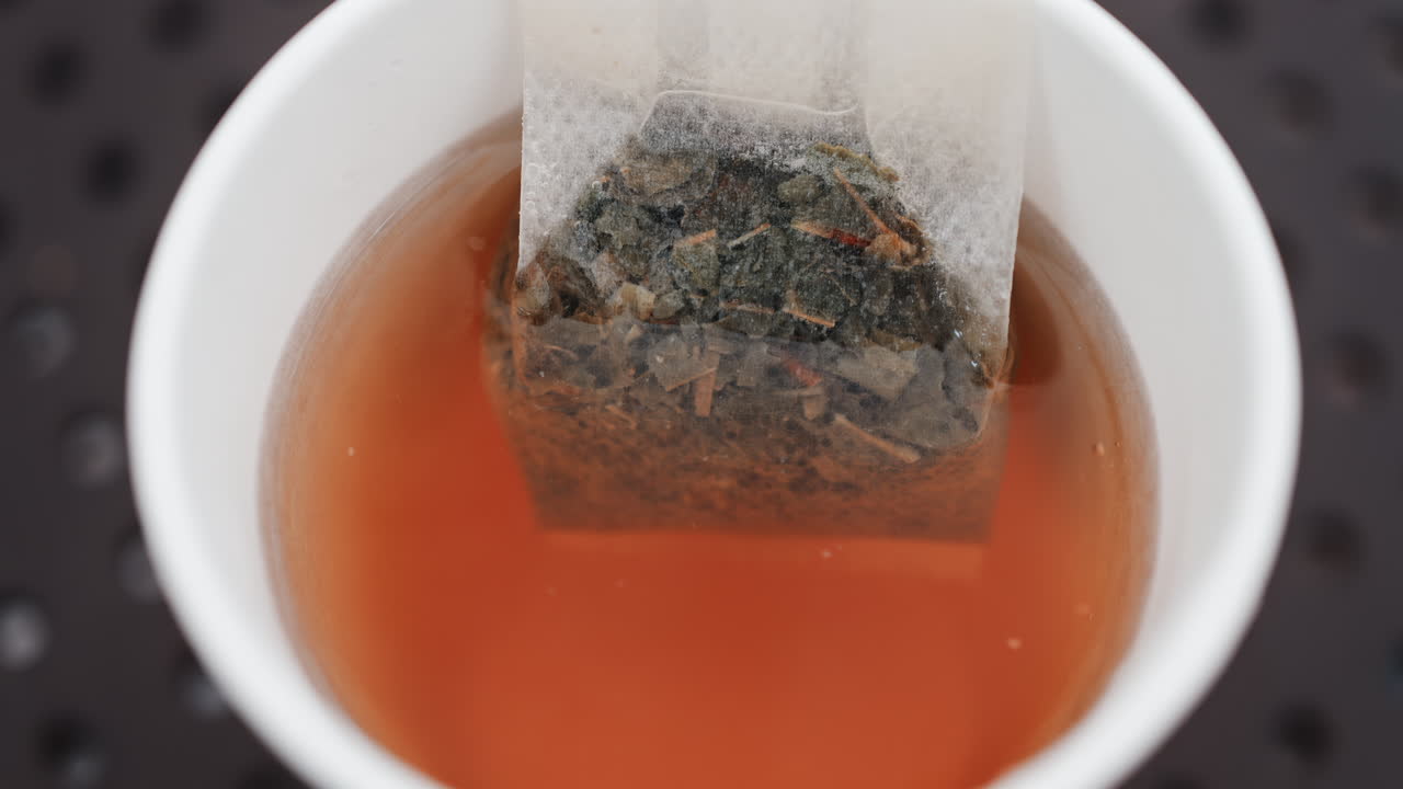 Close up of a tea bag steeping in hot water, releasing rich colour and aroma