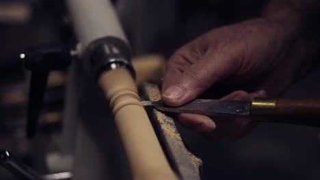 Carpenter-male-hands-cutting-wooden-knob-out-of-wood-piece-spinning-on-machine-using-chisel,-close-up-shot.-Slow-motion.-Side-view