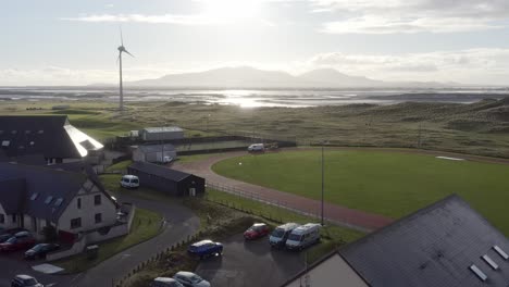 Ascending-drone-shot-moving-from-the-UHI-college-campus-and-the-track-and-pitch,-to-the-distant-beach,-mountain-range-and-the-nearby-wind-turbine