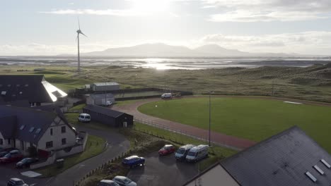 ascending drone shot moving from the uhi college campus and the track and pitch, to the distant beach, mountain range and the nearby wind turbine