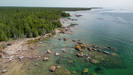 aerial pan to up forested coastline with large boulders and cleear water, lake huron, michigan