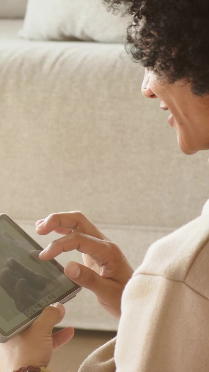 Video verticale: Uomo in dolcevita che tocca lo schermo illuminato, naviga sul tablet sul divano di casa, spazio per il testo.