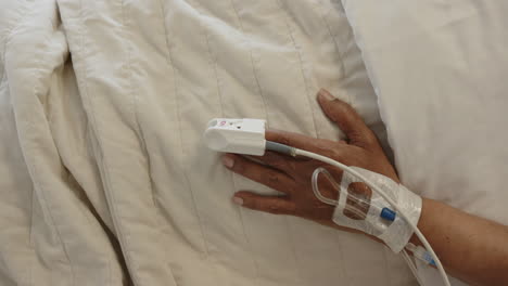 hand of african american senior female patient sleeping in bed in hospital room, slow motion