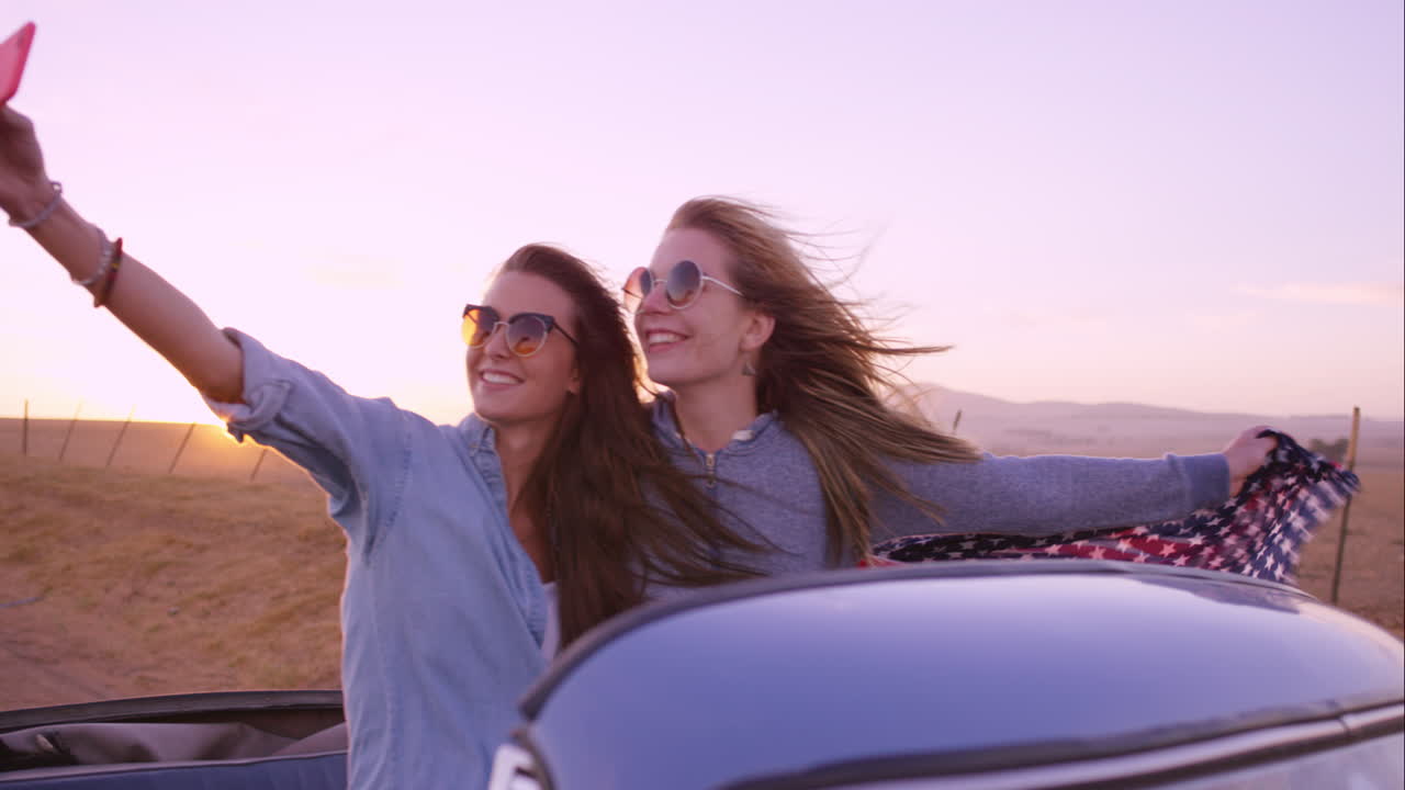 hermosas amigas tomando selfies en un viaje por carretera al atardecer con un coche antiguo