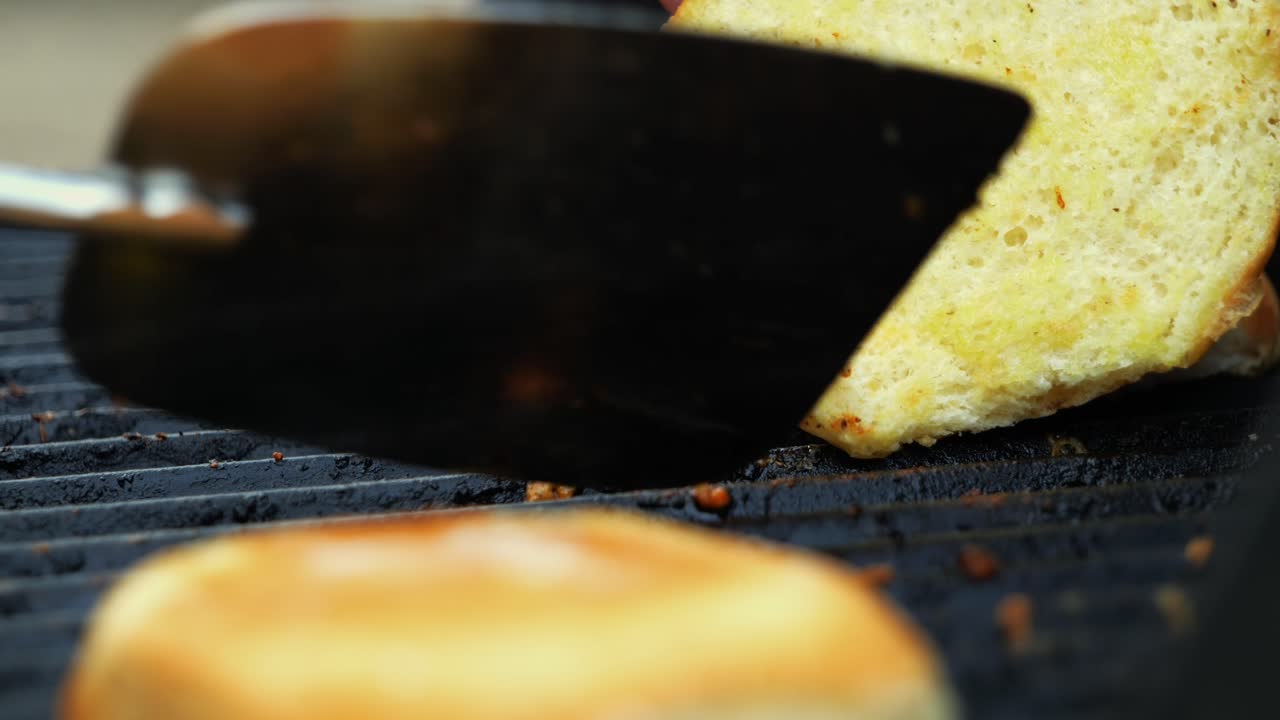Barbecuing burger patty buns on electric grill and flipping them over with meat remnants and bubbling cheese left low angle freshly placed on grill - in Cinema 4k (30fps slow from 60fps).