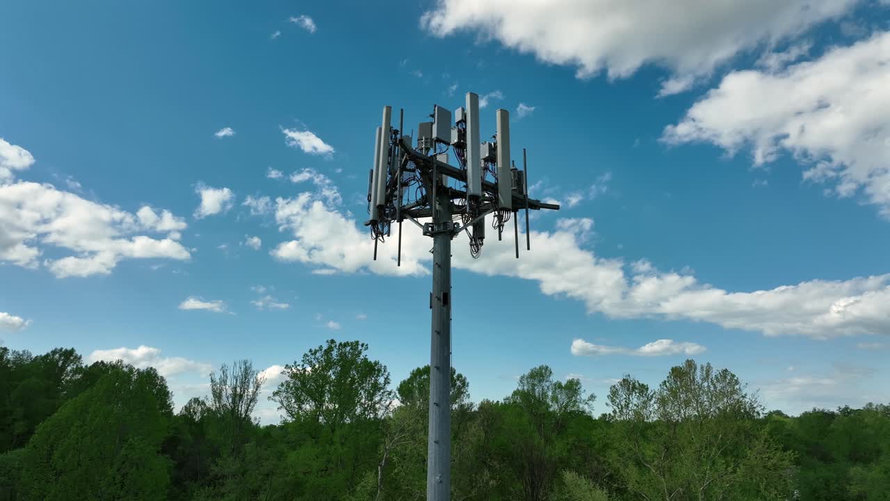 Aerial orbit shot of telecommunication tower in scenic area of United States. Blue sky and white clouds at sky. Bottom up shot. Signal of antennas to cityscape.