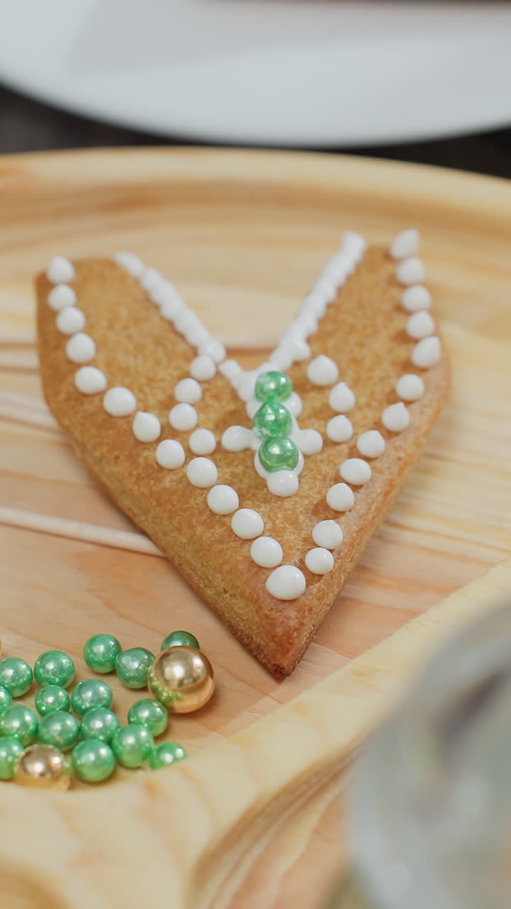 Close-up of green and gold decorative beads scattered around decorated cookies on a wooden tray, cookie adorned with white icing and beads in a beautiful, artistic display