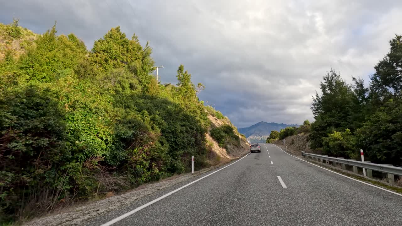 Vehicle travels winding mountain highway, lush greenery, overcast sky, daylight, forward-facing dashboard camera view