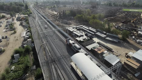 Suburban-train-departing-from-the-station-in-industrial-city-area-aerial